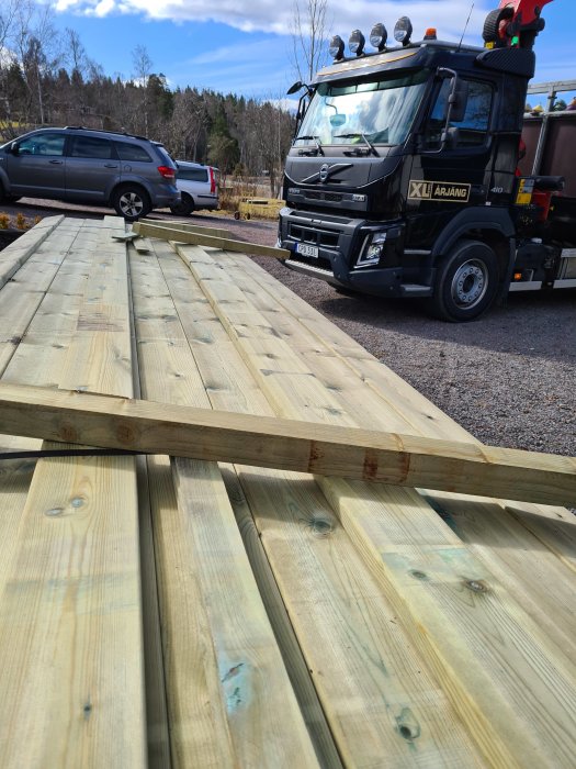 Leverans av nya träplankor för byggprojekt vid en bostad, med en lastbil i bakgrunden.