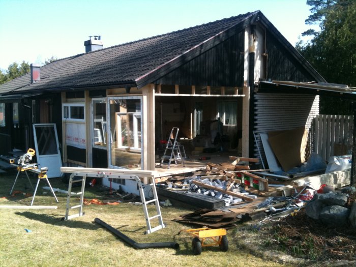 Hus under renovering med byggmaterial och verktyg utspridda framför fasaden.