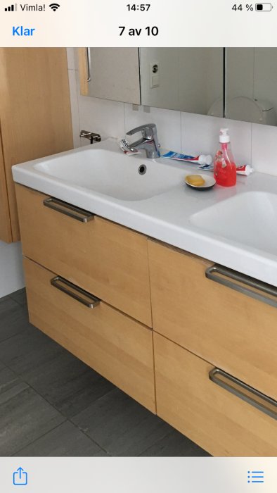 Badrumsskåp i ekfärg med fyra lådor och handfat ovanpå, synliga nötningstecken, vardagsprodukter på diskbänken.