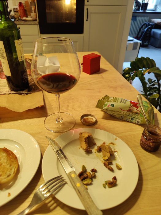 Ett glas rött vin, rester av foie gras på tallrik med pistagenötter, och en vinglasflaska.