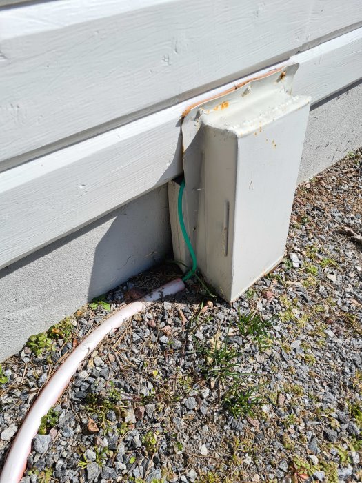Oskyddade kablar löper ut från en elanslutningslåda vid en husvägg och ner på grusmark.