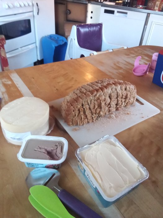 Hembakat bröd på skärbräda, smör och leverpastej på köksbord redo för frukost.