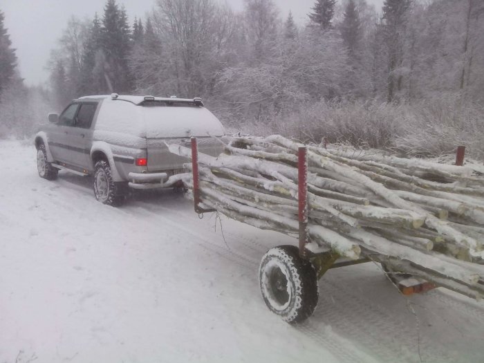 Pickup med en timmervagn full av ved på en snöig väg.