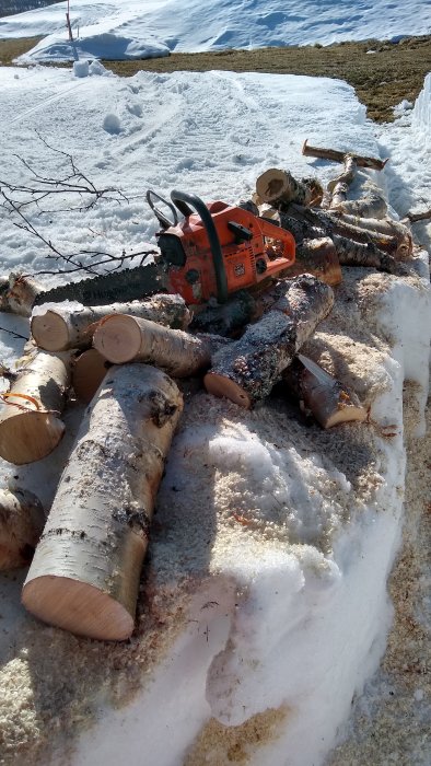 Husqvarna motorsåg på nedsågade trädstammar omgivna av snö.