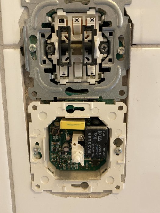 Öppet eluttag med synlig elektronik och anslutningar i en vit vägg.