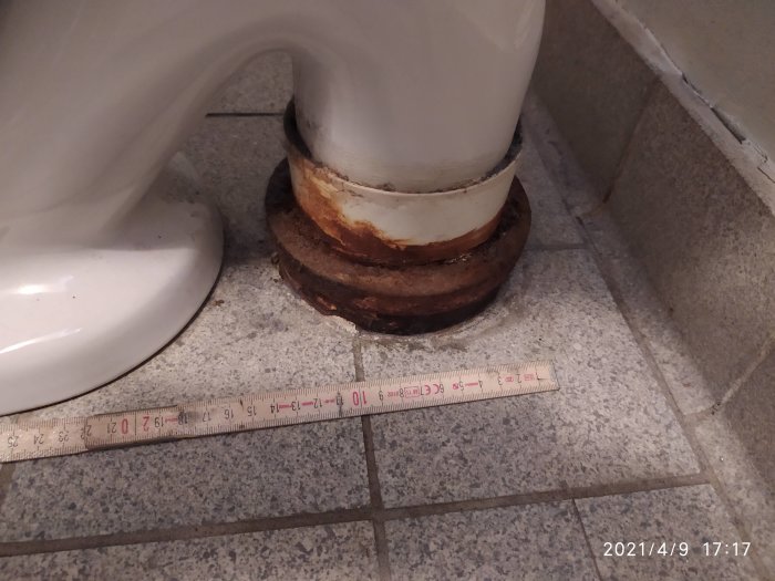 Gamla toalettstolens öppna S-lås och anslutning till golvavlopp, mäter för byte.