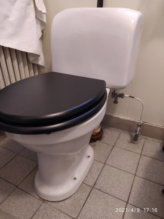 Toalettstol med svart sits, påfyllningsventil och avlopp i golvet i badrum behöver underhåll.