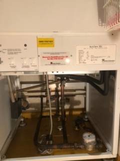 Värmepump och rörinstallationer under, inspektionslucka på golv i tvättstuga.