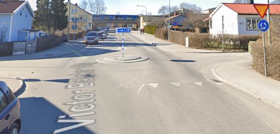 Rondell med vägskyltar, vägmarkeringar för avfarter och en blå buss i bakgrunden.