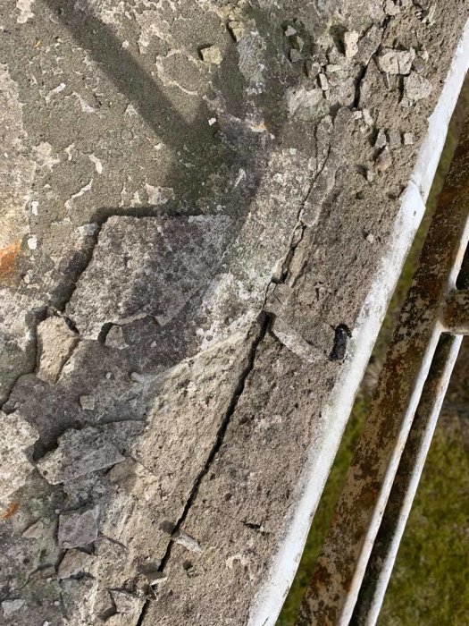Närbild på en sliten balkongyta med synliga sprickor och nedbrytning bredvid ett gammalt vitmålat räcke.