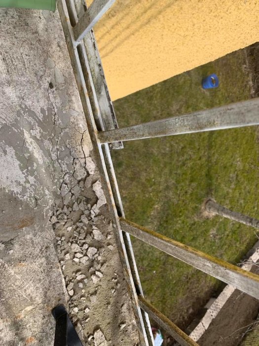 Nedgånget balkonggolv med spruckna betongbitar och gammalt metallräcke, behöver renovering.