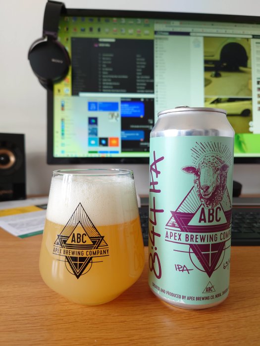 Ölglas med skum topp och Apex Brewing IPA-ölburk framför en dator med skärmar som visar programvara.