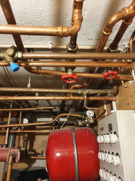 Komplex installation med kopparledningar, ventiler och en röd expansionskärl kopplat till en bergvärmepump.