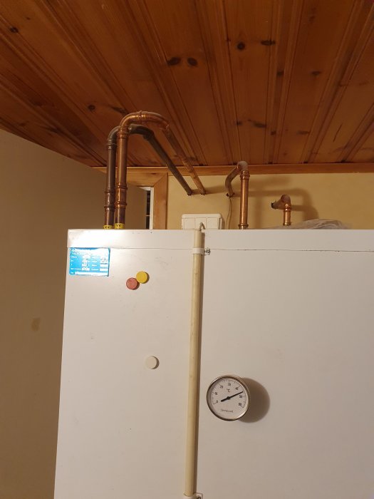 Bergvärmepump i ett hus med synliga rör och en termometer på framsidan.