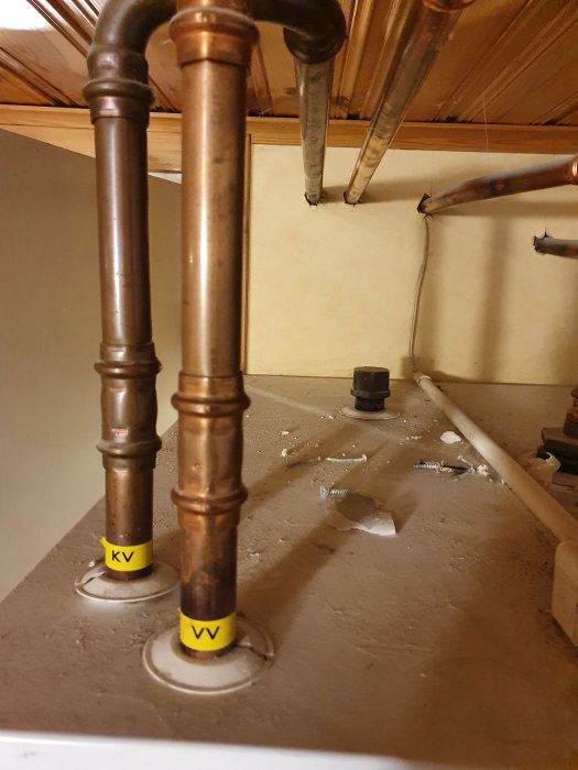 Kopparrör och installationer i ett värmesystem märkta med "KV" för kallvatten och "VV" för varmvatten.