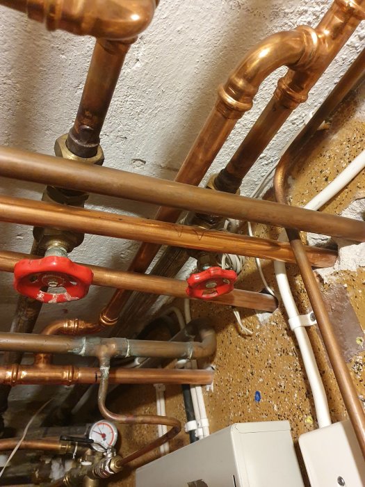 Sammanvävning av kopparledningar och ventiler, varav några märkta med VV för varmvatten, i ett pannrum.