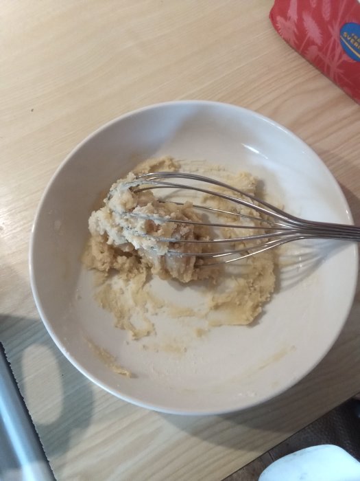 En skål med halvtillagad flötgröt och en visp på ett träbord.