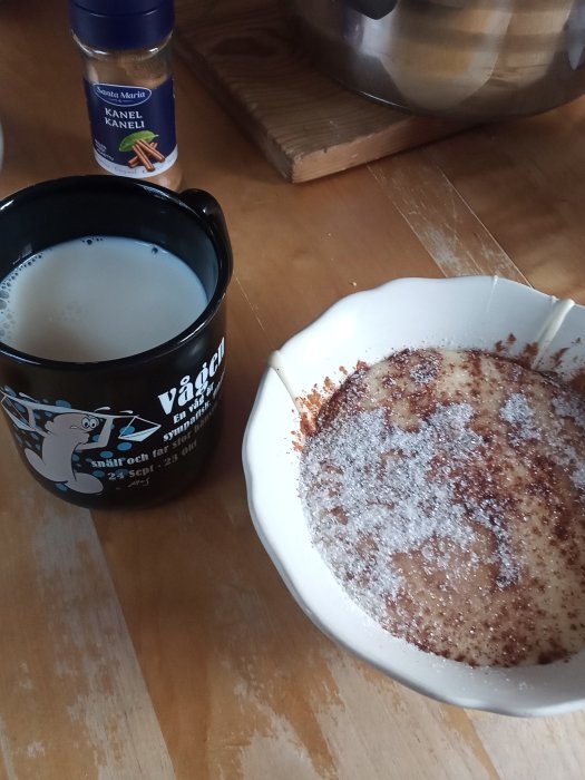 Hemlagad flötgröt i vit skål med kanel och socker ovanpå, bredvid en kopp mjölk och en kanelburk.