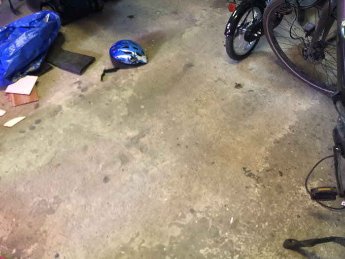 Slitet betonggolv i garage med skador och en cykel till höger.