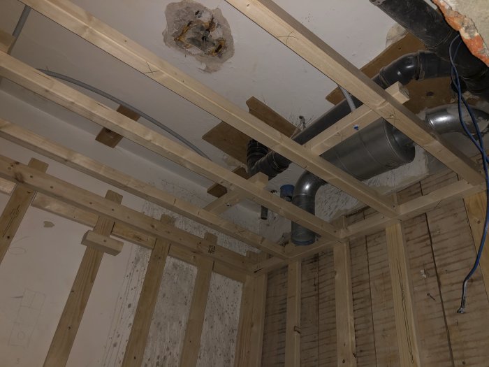 Öppet tak med exponerade träbjälkar och synliga VVS-installationer efter badrumsrenovering.