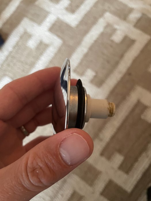 Närbild på en hand som håller en sliten badkarsventil med synliga gängor och delvis synligt märke.