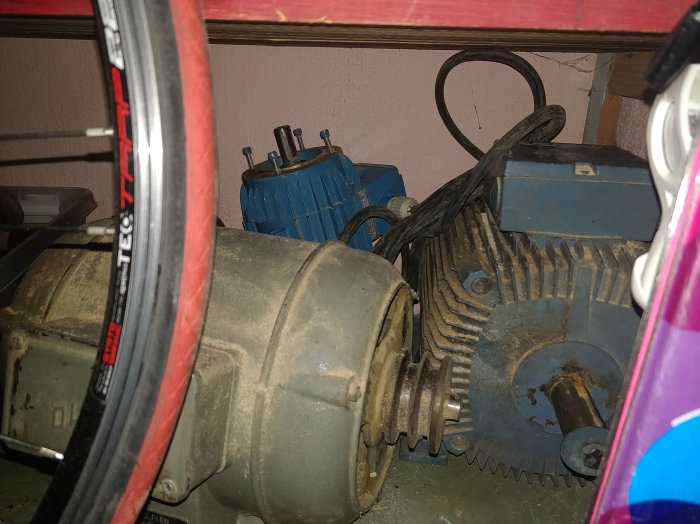 Samlingsbild på olika elektriska motorer med axlar och remhjul i en källare.