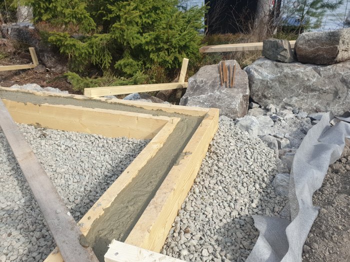 Nygrundad betongplatta med träformar omgiven av grus och sten, i ett pågående byggprojekt.
