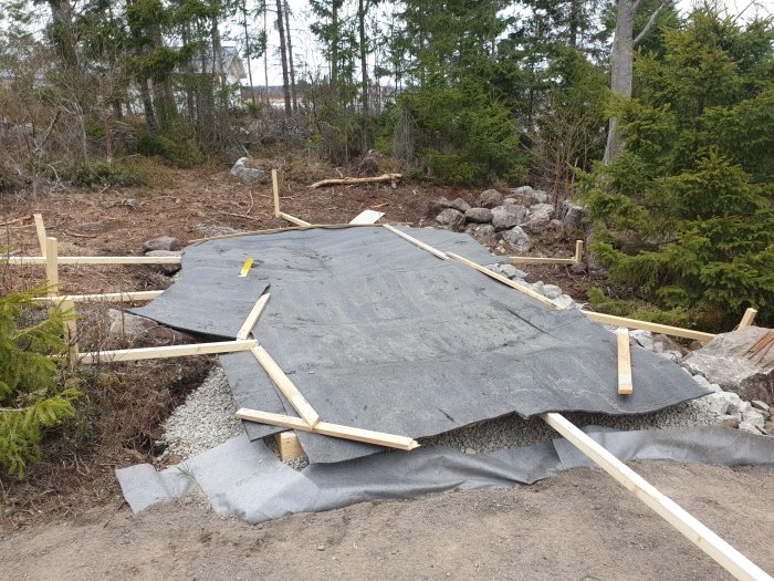 Nyutgjuten betong täckt med grå betongtäckmatta för härdning, inramad av träformar i utomhusmiljö.