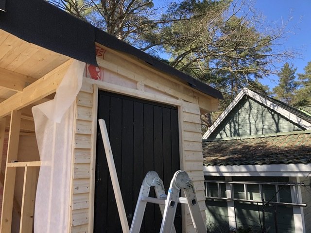 Nybyggt träskjul med halvfärdigt tak och en stege, detaljarbete för inpassning av takpanel.