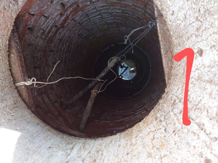 Gammal brunn med öppning och kablar, möjlig vattenbrunn, markerad med en röd siffra 1.