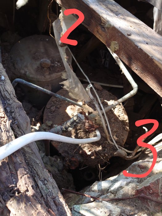 Bild av potentiell vattenbrunn märkt med siffran 2 och en okänd anordning märkt med 3, bland rör och trasiga plåtdelar.