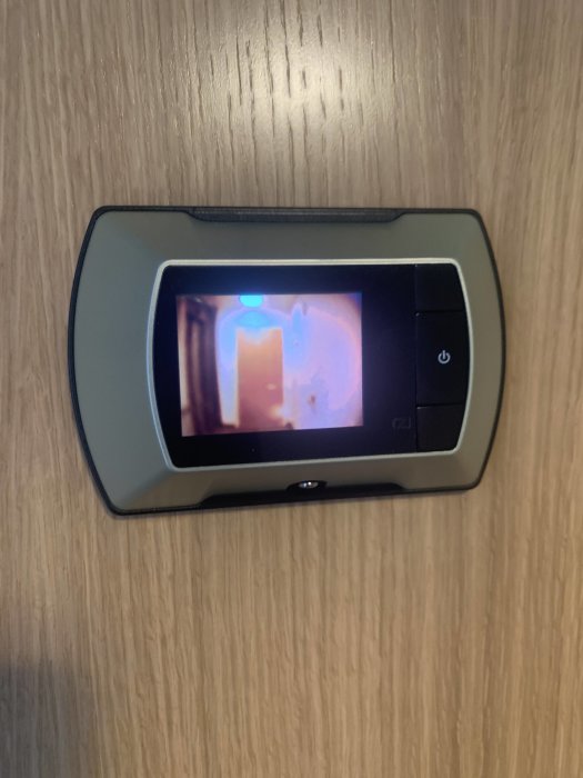 Oskarp bild av ett elektroniskt tittöga monterat på en dörr, visar suddig bild på skärmen.