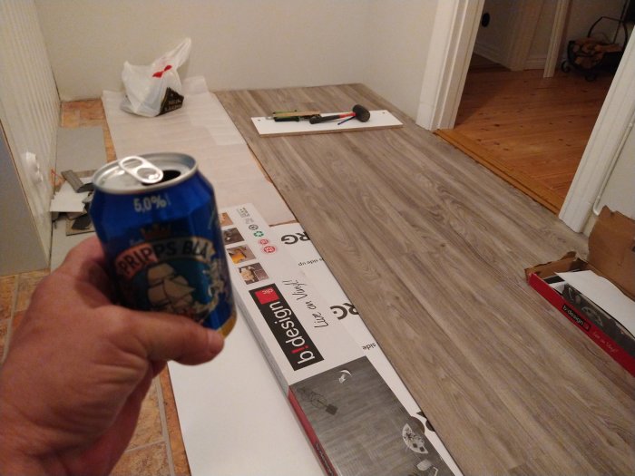 Person som håller i en ölburk med nylagt laminatgolv i bakgrunden.