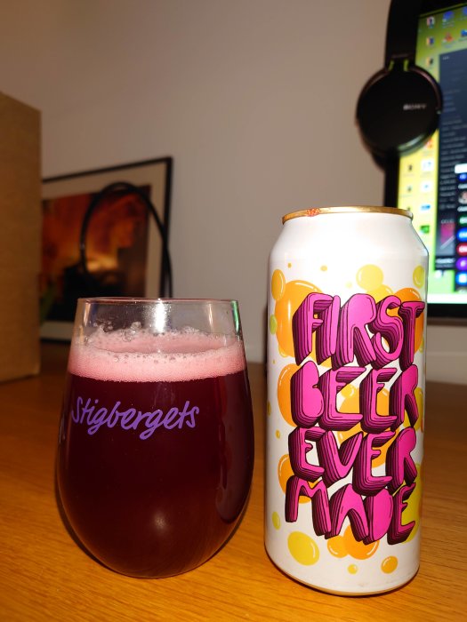 Ölglas med rosa skum och körsbärsfärgad öl bredvid en burk med texten "FIRST BEER EVER MADE".