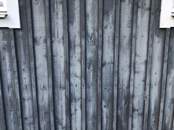 Gråmålad stående träpanel med ojämn färgflamighet, vilket ger ett fläckigt utseende.