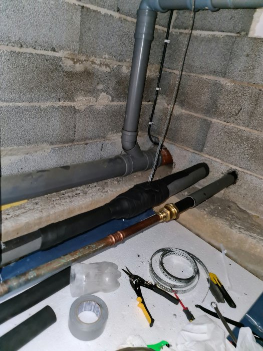 Isolerade VVS-rör med tejp i en krypgrund, verktyg och material synliga på golvet.