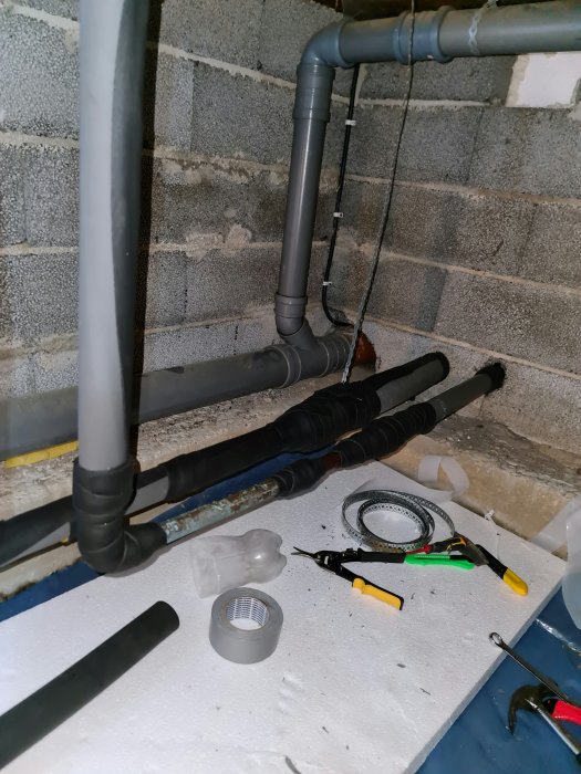 Isolerade rör med tejp och verktyg i en krypgrund under reparation.