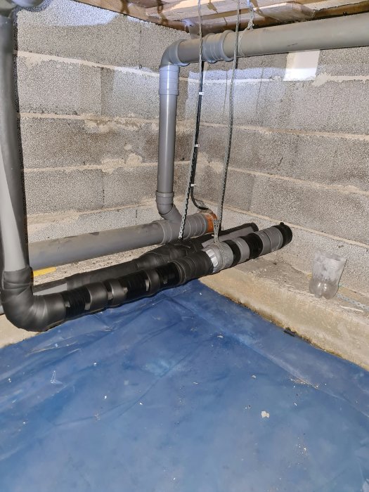 Isolerade värmerör med tejp och isoleringsmaterial i krypgrund med synlig kondens och mätverktyg.