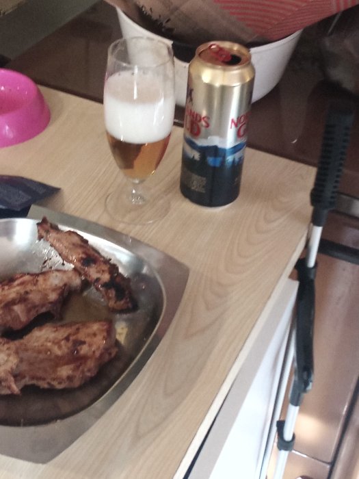 Grillade revbensspjäll på en tallrik, ett glas öl och en ölburk vid sidan om en grilltång på köksbänken.