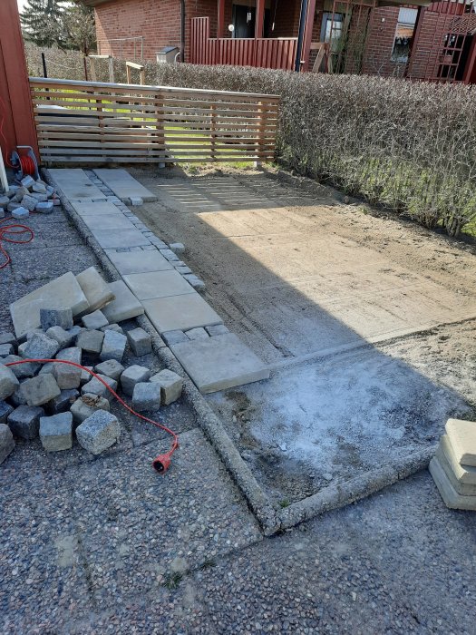 Nybyggd stenlagd yta för cykelparkering brevid en uppfart med betongplattor och lösa stenar.