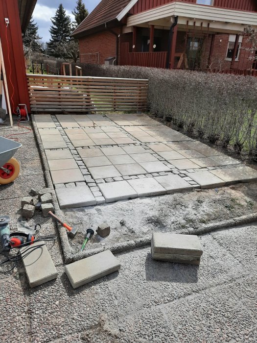 Ny stenlagd yta för cykelparkering med betongplattor vid en uppfart, verktyg och oanvänt material syns.