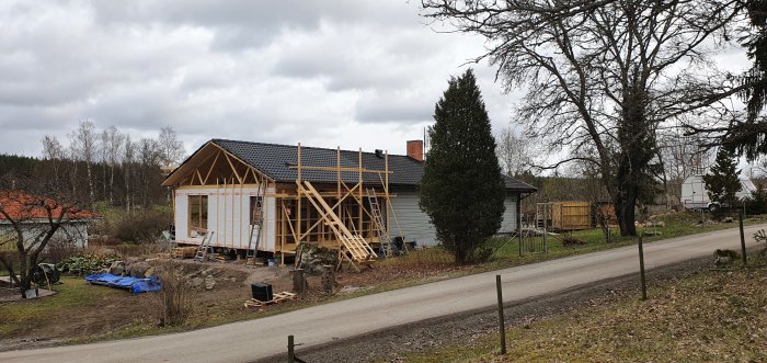 Hus under renovering med nästan färdiglagt tak och återanvända takpannor i en lantlig miljö.