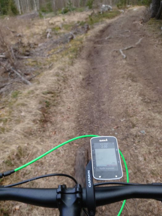 Cykelperspektiv av en skogsstig med en GPS-cykkeldator fäst på styret.