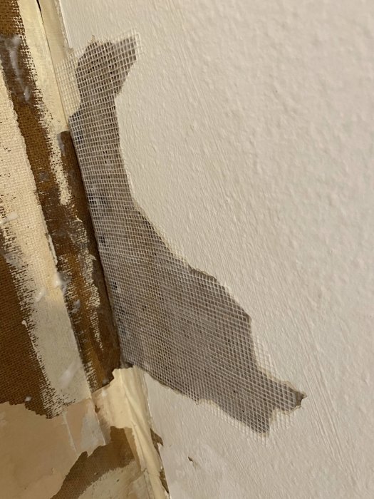 Avsliten tapet som avslöjar nätarmering och delar av en vägg under renoveringsarbete.
