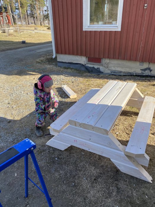 Barn i färgglada kläder står bredvid ett hemmagjort bänkbord av trä i en trädgård.