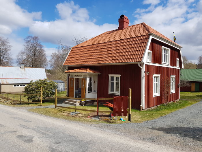 Röd stuga med taktäckning i tegel och pågående arbete med en torkställning i trä på sluttande gräsmark.