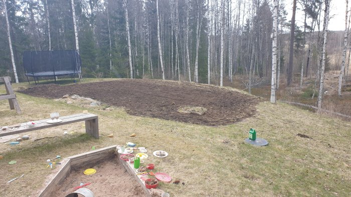Nyfräst mark i en trädgård för projekt, med leksaker och sittplatser i förgrunden.