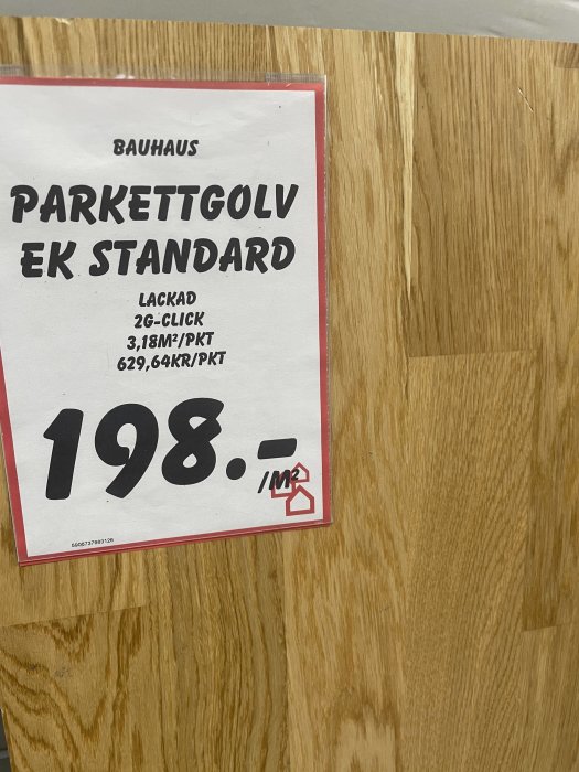 Närbild på en skylt från Bauhaus som visar "Parkettgolv Ek Standard" med pris och en bit av parkettgolvet i bakgrunden.