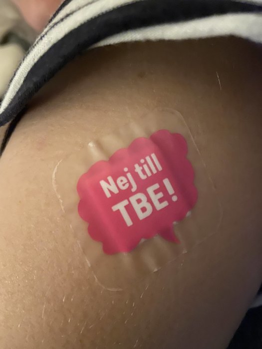 Plåster på en arm med texten "Nej till TBE!" i rosa och vit färg.