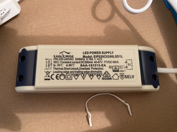 LED-strömförsörjning märkt med SELV och olika säkerhetsikoner på en källarhylla, omgiven av kablar.